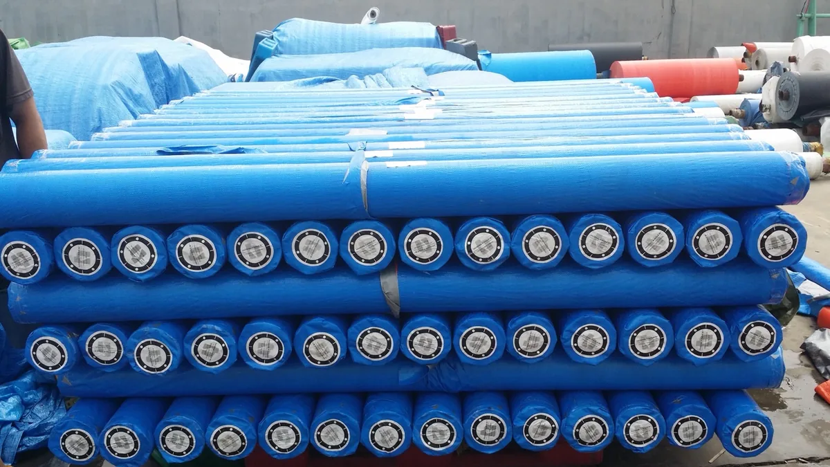 Rouleaux emballés en bleu et empilés, avec étiquettes circulaires aux extrémités.